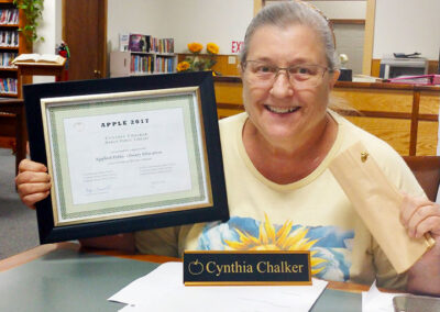 Cynthia Chalker holding up her framed certificate and pin.